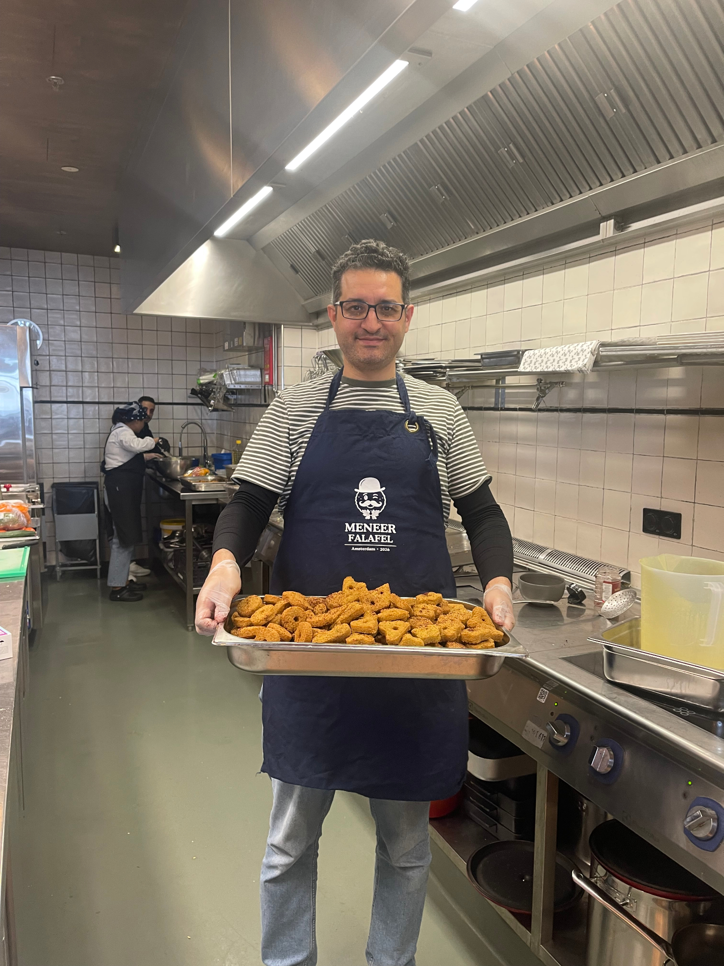 Diaa Alyasin, de oprichter van Meneer Falafel, glimlachend met een schaal verse falafel in de keuken